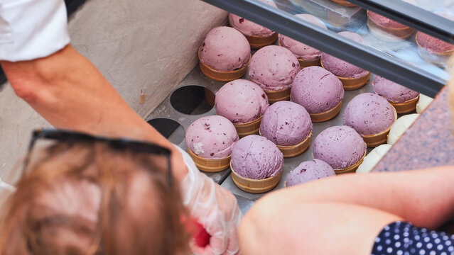 Ice cream shop worker serving berry sorbet scoops in waffle cones to a customer