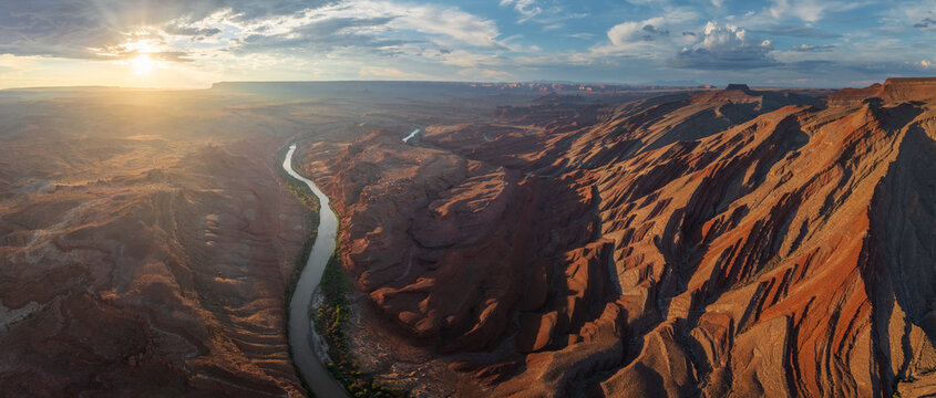 Aerial view of the winding river cuts through the arid landscape where the sun casts long shadows and paints the cliffs in fiery hues, Mexican Hat, Utah, United States.