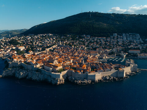 Aerial view of the terracotta rooftops and stone walls of Dubrovnik Old Town meet the azure Adriatic Sea under the gaze of Mount Srd, Dubrovnik, Dubrovnik-Neretva County, Croatia.