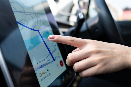 Woman's hand interacts with a modern car's touch screen navigation system for route planning. GPS map, destination, convenient driving technology concept.