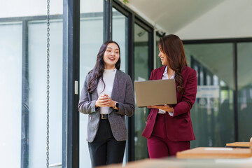 Two Asian businesswomen collegues walking and having a professional discussion, sharing ideas and working together in an office