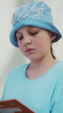 Child reads quietly, eyes focused on book. Soft blue hat and shirt match the calm mood. Smile suggests gentle joy or contentment. Ideal for cozy, educational, or children's scenes