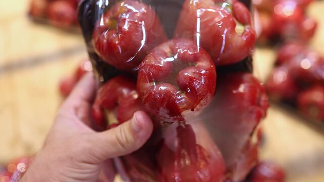 Close up of a hand holding a pack of fresh rose apples in a supermarket. Customer choosing organic wax apple fruit in a grocery store. Healthy nutrition and tropical ingredient concept.