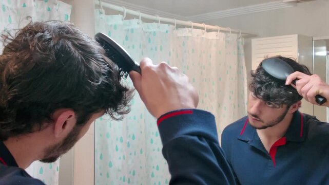 man looking at mirror combing hair with hairbrush getting ready in bathroom