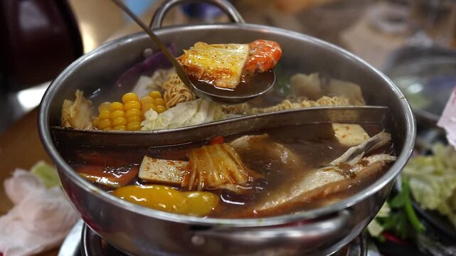 Close up of traditional Vietnamese hot pot Lau boiling on a table in Vietnam. People cooking soup with seafood, noodles and vegetables in a split metal pot. Authentic local street food dining concept.