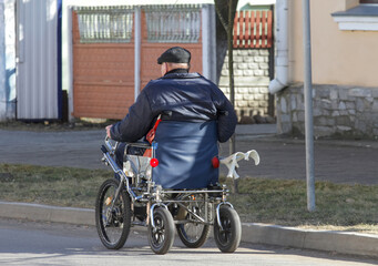 Fototapeta premium Senior man uses wheelchair on city street by old buildings in daytime