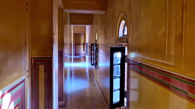 A narrow interior corridor inside a Rajput palace at Amber Fort, Jaipur, showing long painted walls with traditional Rajasthani border designs, small arched windows, and wooden doors.