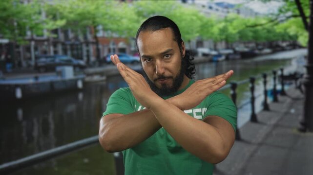 Man wearing volunteer t shirt crossing arms in x gesture on canal street in amsterdam; rejection boundary resolve.