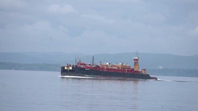 Aerial view of tugboat pushing cargo barge on river with green hills. strategic point for oil transportation and other cargo through the ocean. 
