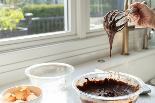 Chocolate brownie batter dripping from whisk with egg shells in kitchen