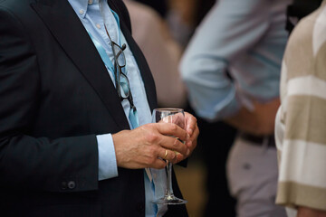 Close-up of a business event guest holding a champagne glass during a corporate reception or networking gathering. © Alexey Bakharev