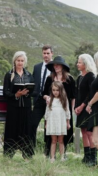 Funeral, family and reading bible at cemetery for burial, memorial service or farewell ceremony. People, religion and officiant with book at graveyard for grief, death and faith with generations