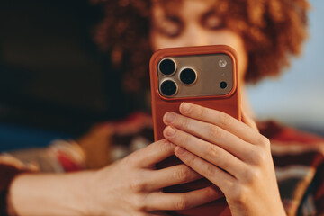 Woman with curly hair wearing a rainbow sweater smiling while holding smartphone, casual lifestyle...