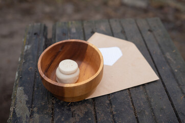 Wooden bowl with soap figurine and envelope on rustic surface