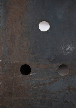 Imagen vertical de de una barra de metal con tres huecos y oxido