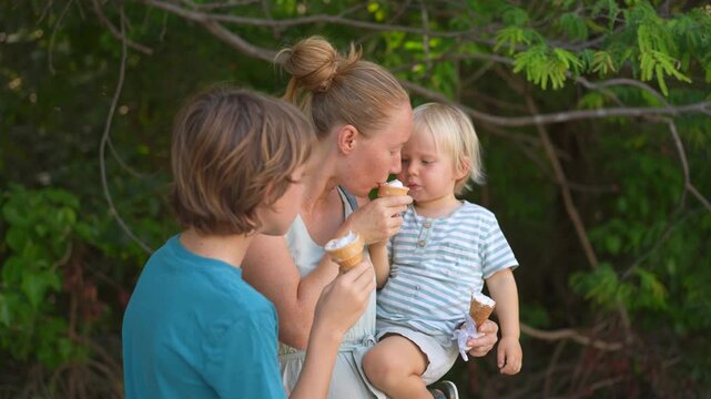 Young mom spending quality time with her two sons in a lush green park, enjoying nature, laughter, and joyful family bonding moments outdoors.