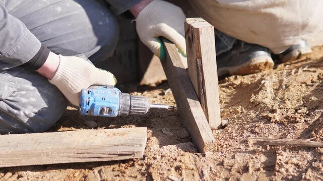 Worker Placing Timber Stake And Drilling Into Soil At Construction Layout, Closeup Of Gloved Hands, Small Triangular Stakes And Leveling Action For Foundation Guide Gritty Ground