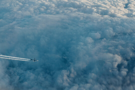 Aerial view of an airplane flying above sea of clouds with long condensation trails.
