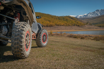Close up of UTV off-road vehicle wheels with red beadlocks on a mountain meadow by a lake. Expedition, extreme adventure travel and overlanding concept in autumn. © ANDREY