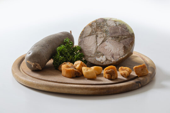 Traditional Czech pork feast: liver sausage (jitrnice), headcheese (tlacenka), and crispy pork rinds on a wooden board with fresh parsley.