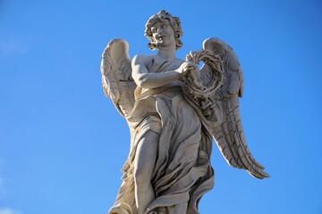 Fototapeta premium A white marble statue of an angel with a crown of thorns depicts a biblical scene on Ponte Sant'Angelo, the landmark angel bridge of Rome, Italy.