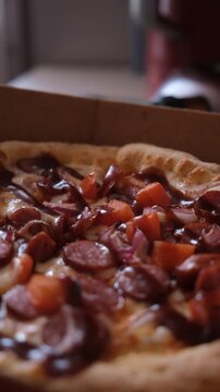 Spicy pizza with chorizo sausages, pelati sauce, mozzarella cheese topped with salami, smoked chicken, garnished with fresh tomatoes and red hot pepper slices. Cardboard box 