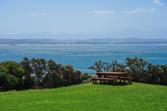 South Africa,Mossel Bay,Bartolomeu Dias Museum Complex,Picnic area overlooking a vast blue sea with distant mountains under a clear sky