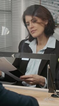 Vertical close-up of anonymous African American businessman checking documents, then submitting paperwork for work visa to Caucasian female officer at embassy counter