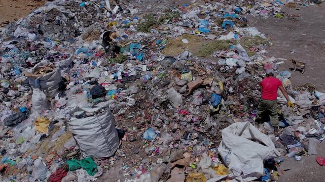 Aerial view of people collecting waste in a landfill with dense garbage accumulation. Scene highlights environmental pollution, waste management, recycling, and human labor.