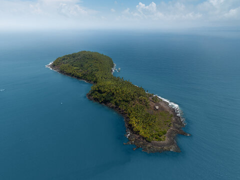 Aerial view of a lush tropical island covered in palm trees and dense vegetation surrounded by the blue waters of the Atlantic Ocean in Iles du Salut, French Guiana.