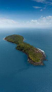 Aerial view of the lush tropical island of Saint-Joseph with dense palm trees and rocky shores surrounded by the blue Atlantic Ocean Iles du Salut, French Guiana.
