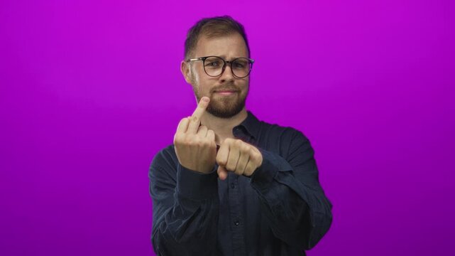 Young man with glasses and beard showing middle finger and clenched fist in magenta studio; defiance attitude.