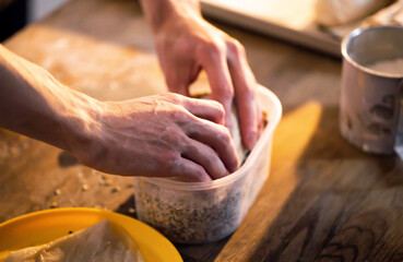 Fototapeta premium Hands of person carefully placing ingredients into plastic container on wooden table for food preparation activity culinary art healthy eating kitchen environment cooking process homemade snack