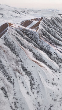 Aerial view of snow-covered rolling hills with rhythmic patterns of ridges and sparse vegetation in Kazakhstan.