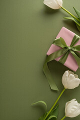 Fototapeta premium Happy Mother's Day vertical composition featuring a pink wrapped present with green ribbon and white tulips on an olive background for greeting cards, social posts and spring gift layouts