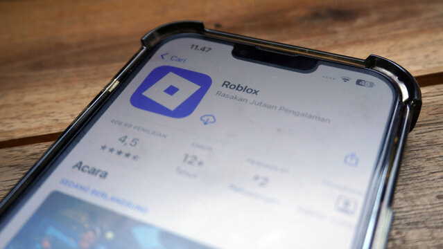 Purwokerto, Indonesia - 25 March 2026: Roblox app store page on smartphone screen placed on wooden table, popular gaming platform editorial closeup, mobile technology concept.