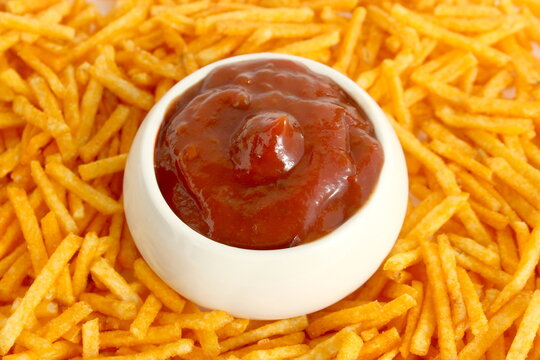 A small bowl of tomato sauce sits surrounded by julienned potato chips.