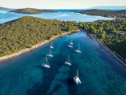 Aerial drone view of flotilla of sailboats and catamaran anchored in sheltered channel between islands, Zadar Archipelago, Dalmatian Coast, Croatia