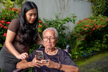 Fototapeta premium Pregnant Woman and Elderly Grandfather Using Smartphone Together in Garden