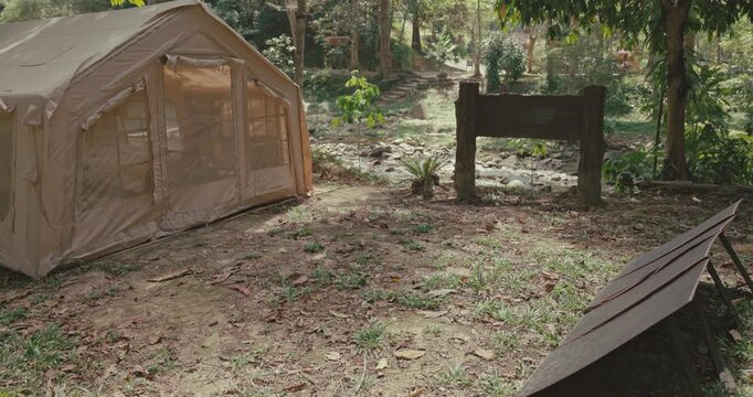 Large canvas tent stands in forest clearing next to portable solar panels. Sustainable camping setup near river for eco-friendly travel and off-grid living.