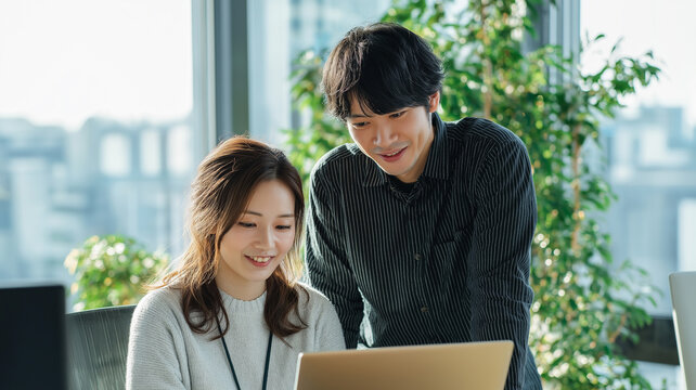 ノートパソコンを見ながら話し合う日本人男女のビジネスチーム（協働・コミュニケーション）