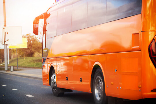 Orange passenger bus movement on urban road at sunset with bright sun flare