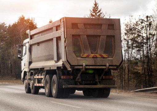 Dirty dump truck driving on highway with another truck ahead, transportation of materials, heavy vehicle operation, industrial logistics, 40-ton truck
