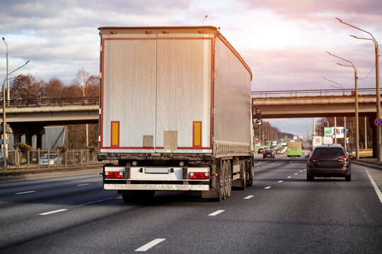 Rear view of long haul truck and trailer on multi-lane highway, transport vehicle carrying goods for logistics industry, driving on road under cloudy sky