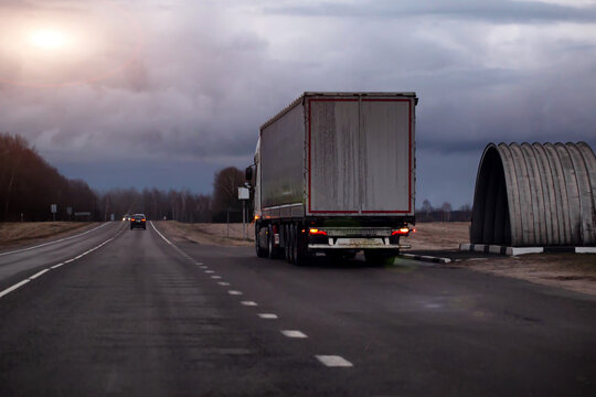 Rear view of large semi-truck traveling on asphalt highway road during overcast day, long distance transport for goods and freight. Copy space for text