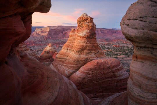 View of sandstone formations ripple with light and shadow under a pastel dawn sky, contrasting with the rugged desert landscape, Page, Arizona, United States.