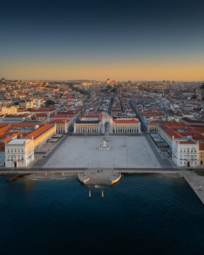 Aerial view of Praca do Comercio with its grand arch and statue, surrounded by historic buildings and the Tagus River under a golden sunset sky Lisbon, Lisbon, Portugal.