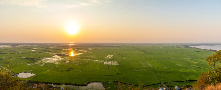 View of the golden sun illuminating the vibrant green rice fields and still waters from a high vantage point, Siem Reap, Siem Reap Province, Cambodia.