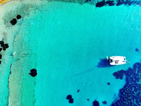 Aerial top-down view of catamaran anchored in vivid turquoise bay with swimmer, Uvala Marculeti, Dalmatian Coast, Croatia