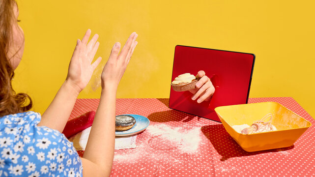 Woman clapping hands as tart appears from tablet screen on flour covered table. Concept of smart kitchen, digital assistant, connected home cooking, and IoT kitchen support.